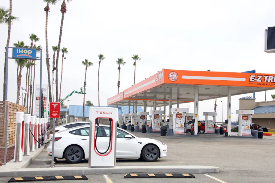 E-Z Trip gas station in Bakersfield, California with orange awning over regular gas pumps and Tesla superchargers with white Teslas charging in foreground.